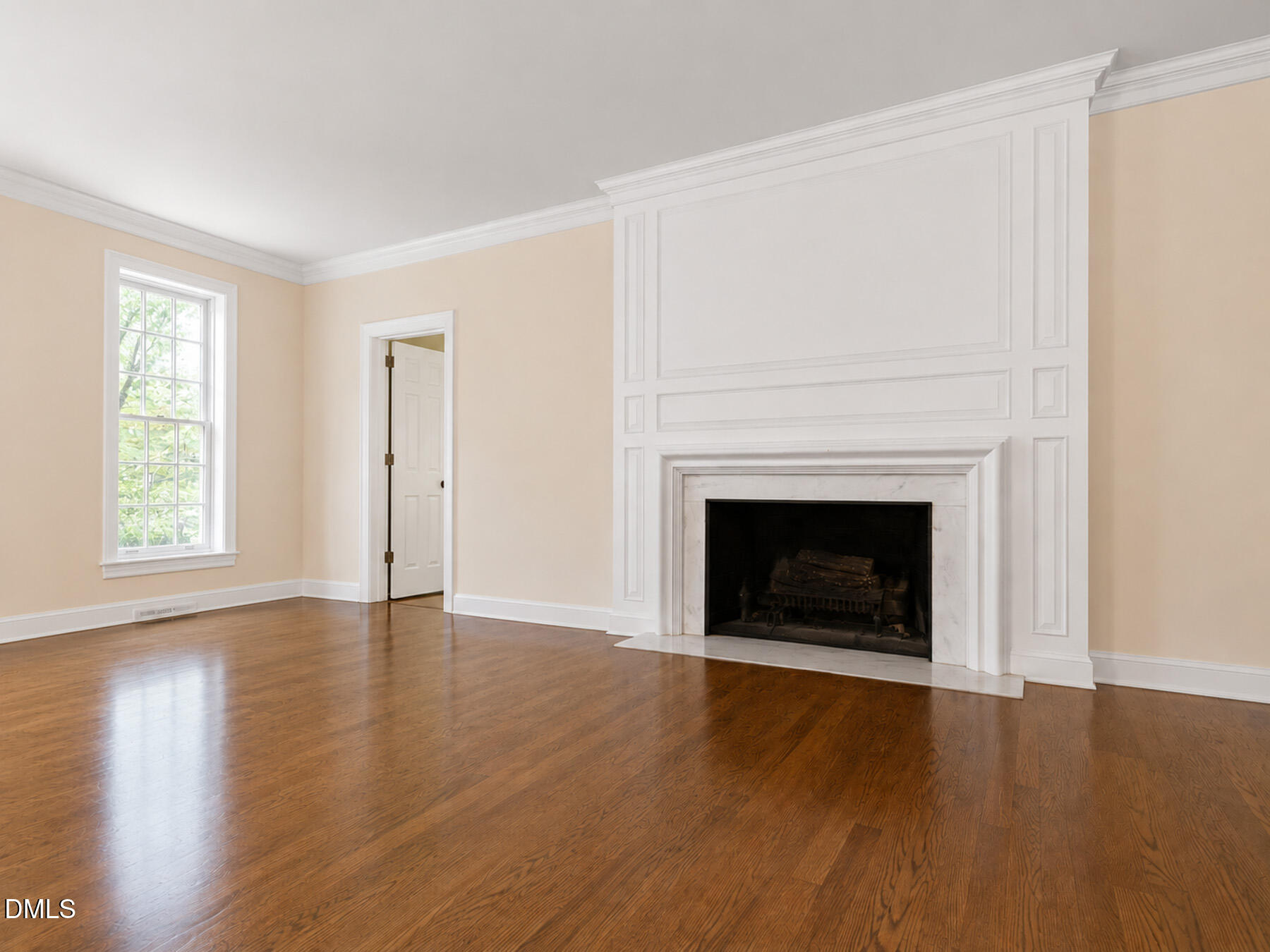 Empty living room with hardwood floors and a large white paneled fireplace.