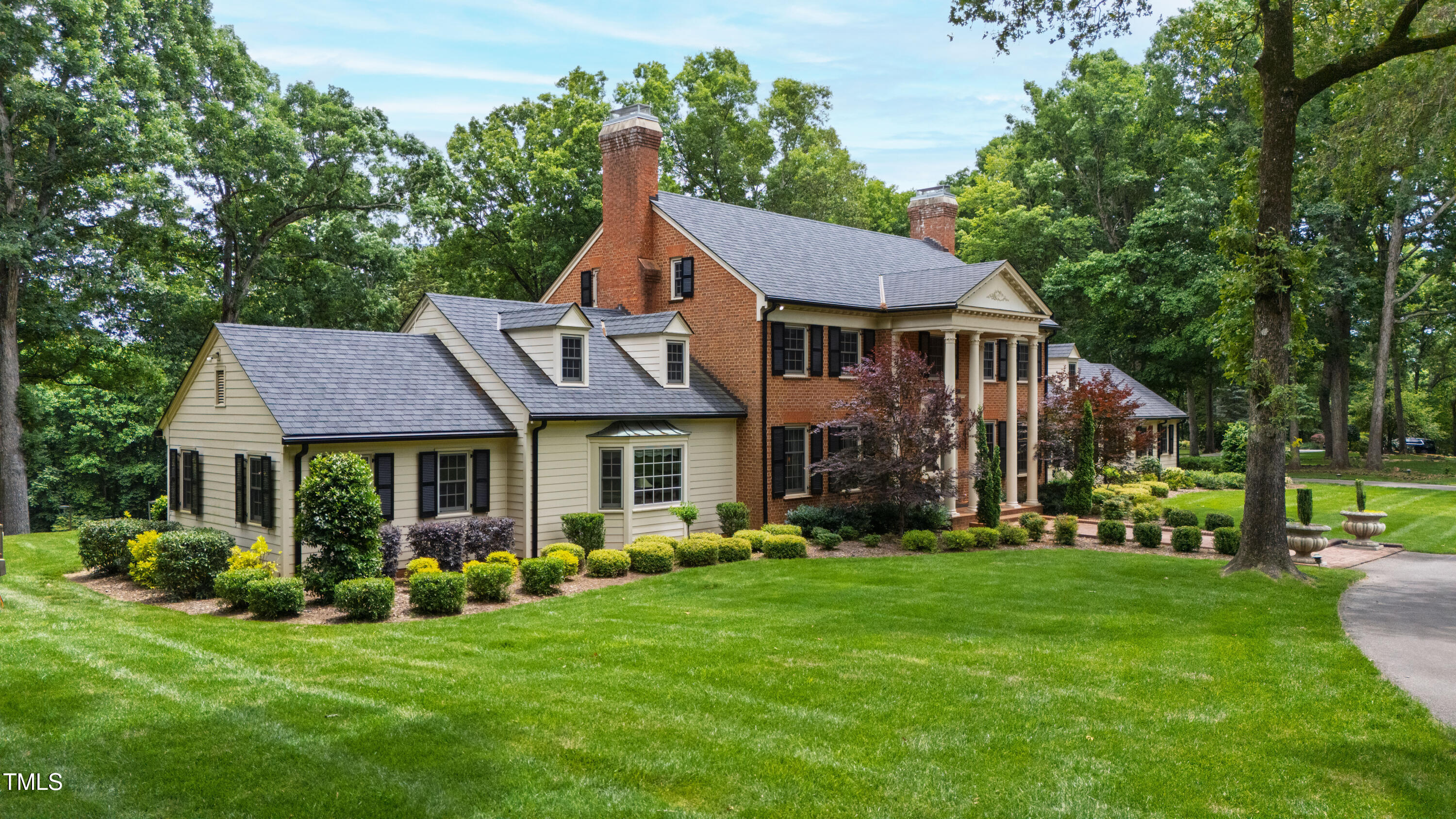 Large brick-and-siding home with a columned porch, landscaped gardens, and a broad green lawn.