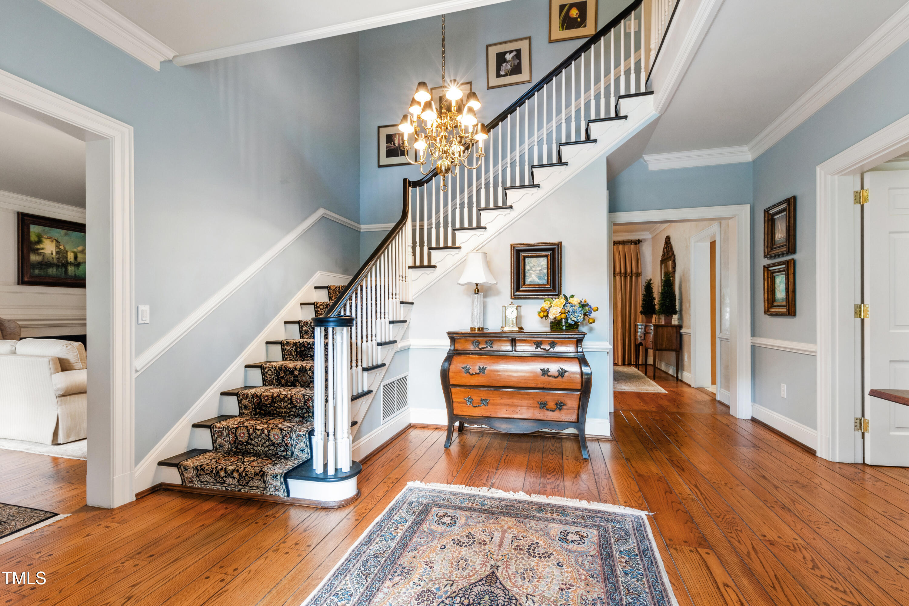 Entry hall with a sweeping staircase, patterned runner, brass chandelier, and polished hardwood floors.