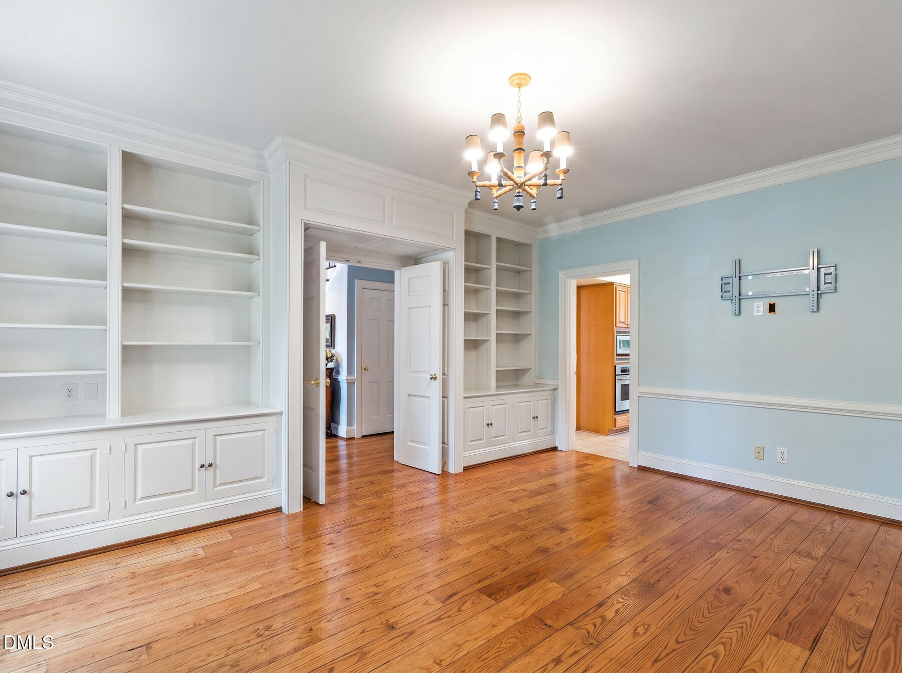 Unfurnished room with built-in white shelving, hardwood floors, and a chandelier.
