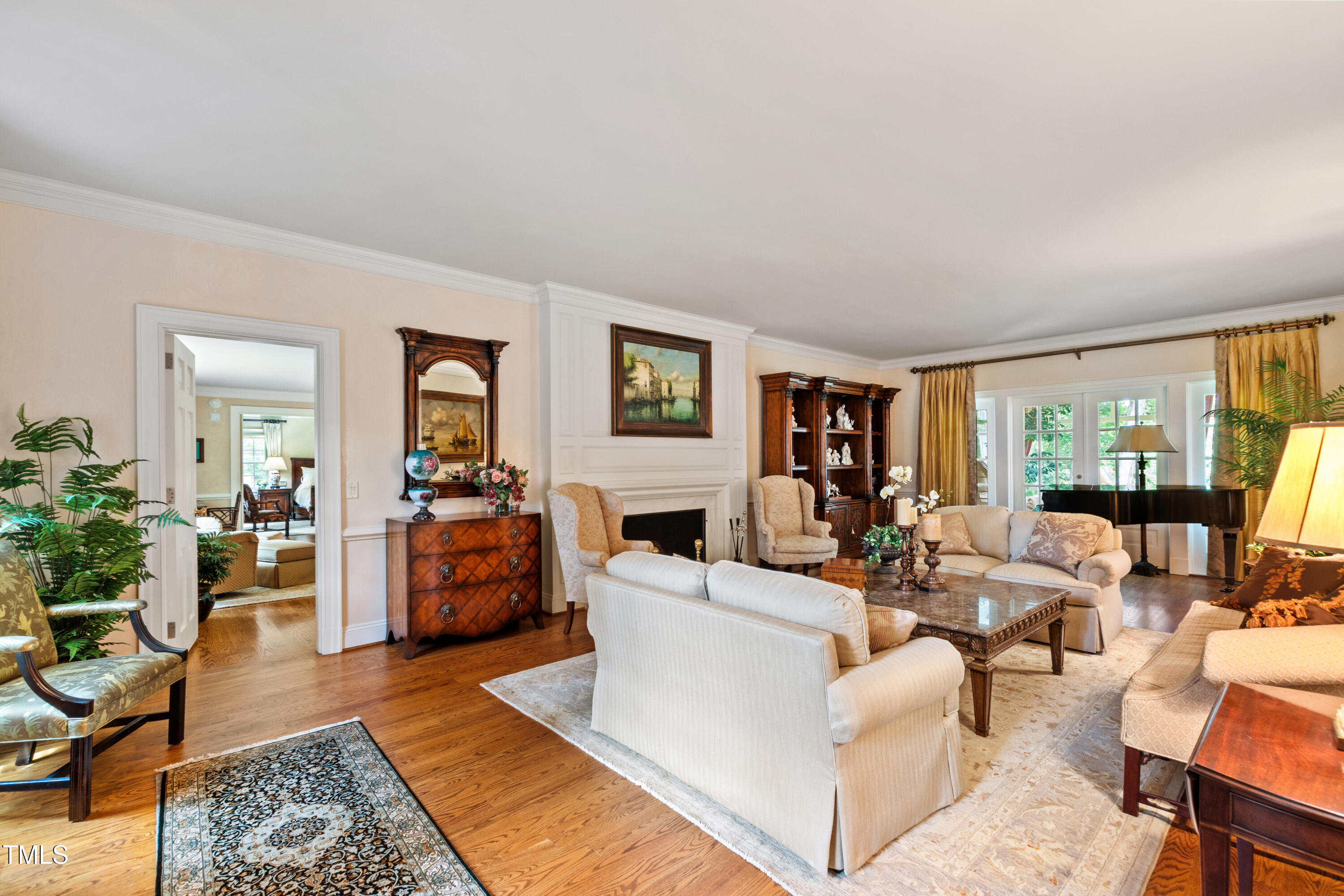 Living room with a paneled fireplace, cream seating, hardwood floors, and a grand piano.