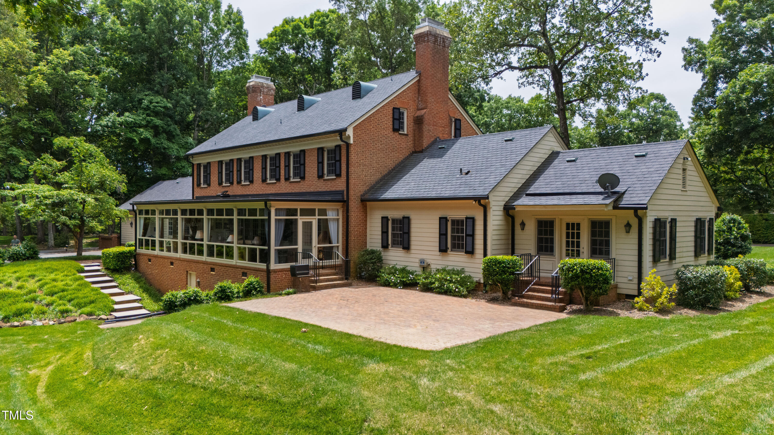 Brick-and-siding home with a glass-enclosed sunroom, broad brick patio, and landscaped lawn.
