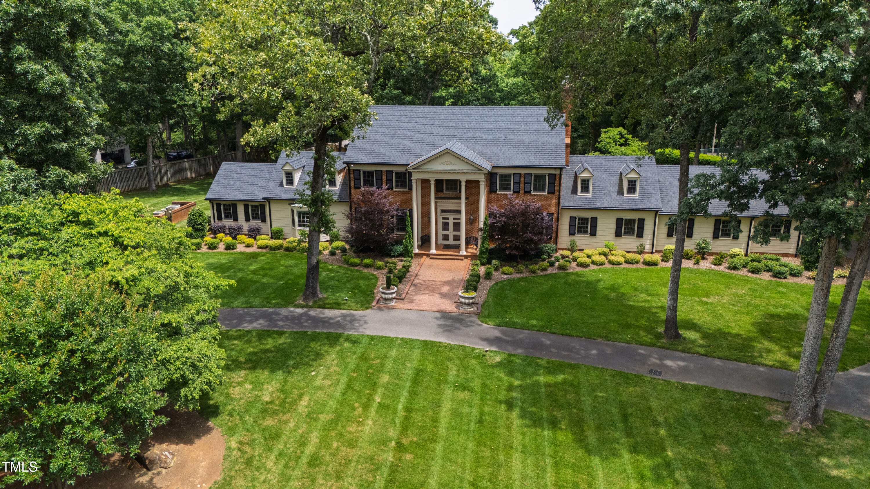 Aerial view of a large home with a brick entry, landscaped gardens, and a tree-lined lawn.