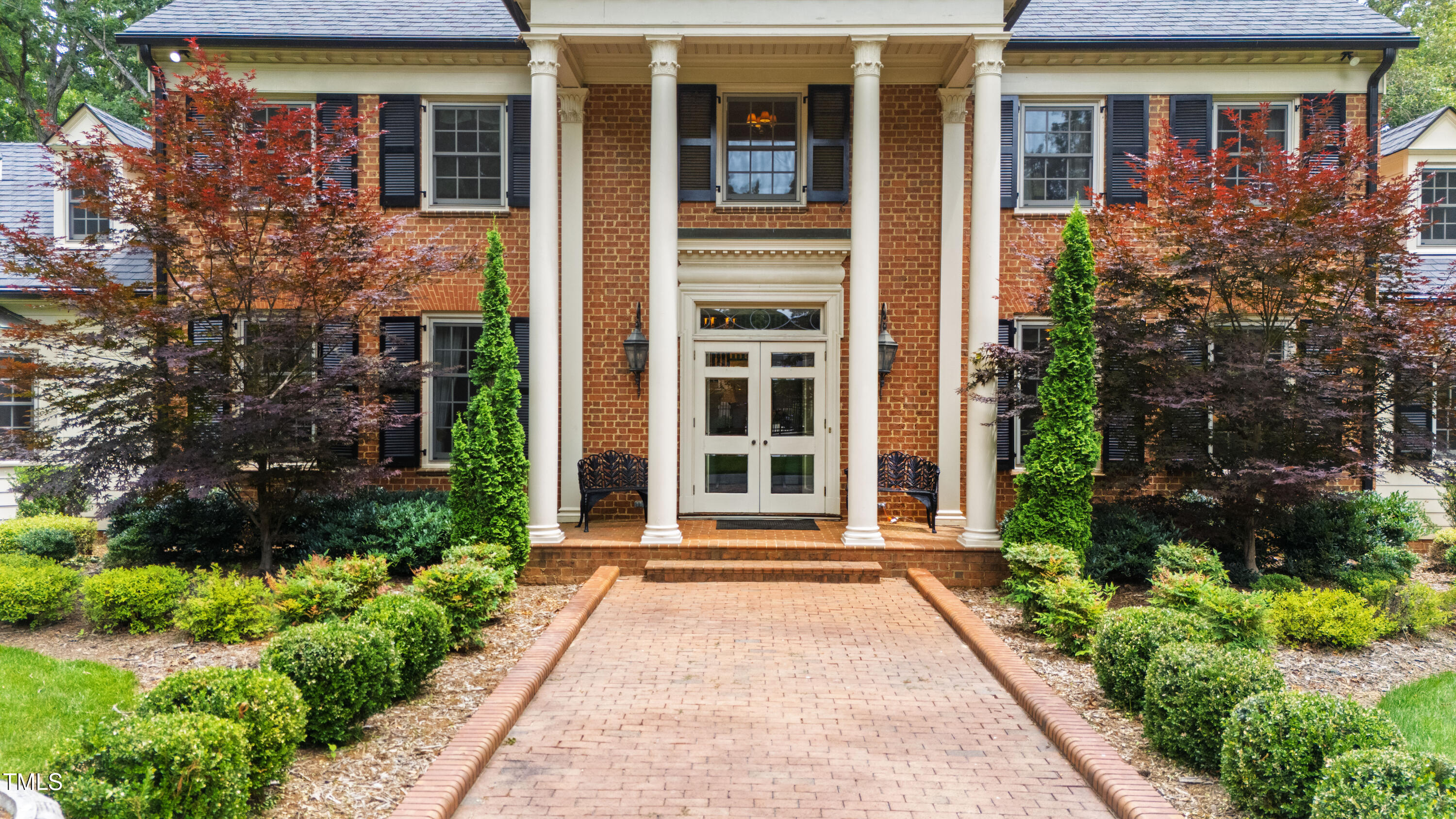 Red-brick home entrance with white columns and a landscaped brick walkway.
