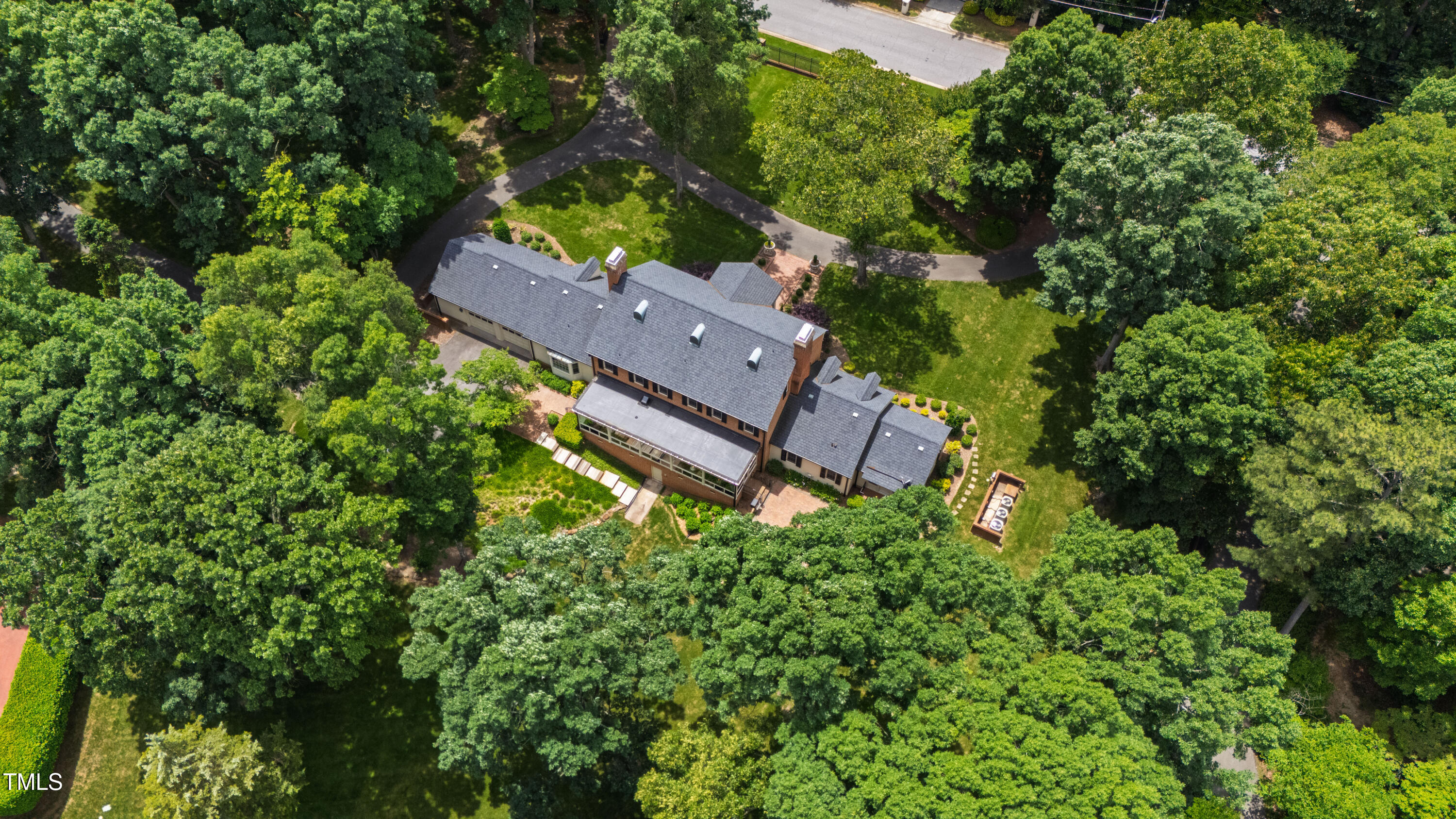 Aerial view of a brick home surrounded by mature trees, lawns, and winding garden paths.