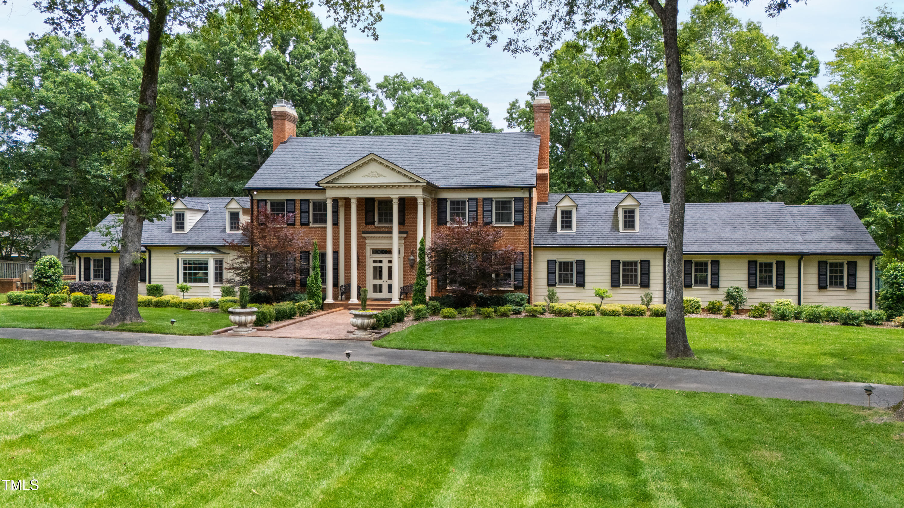 Large brick-and-siding house with a columned entrance, twin chimneys, and a broad lawn.