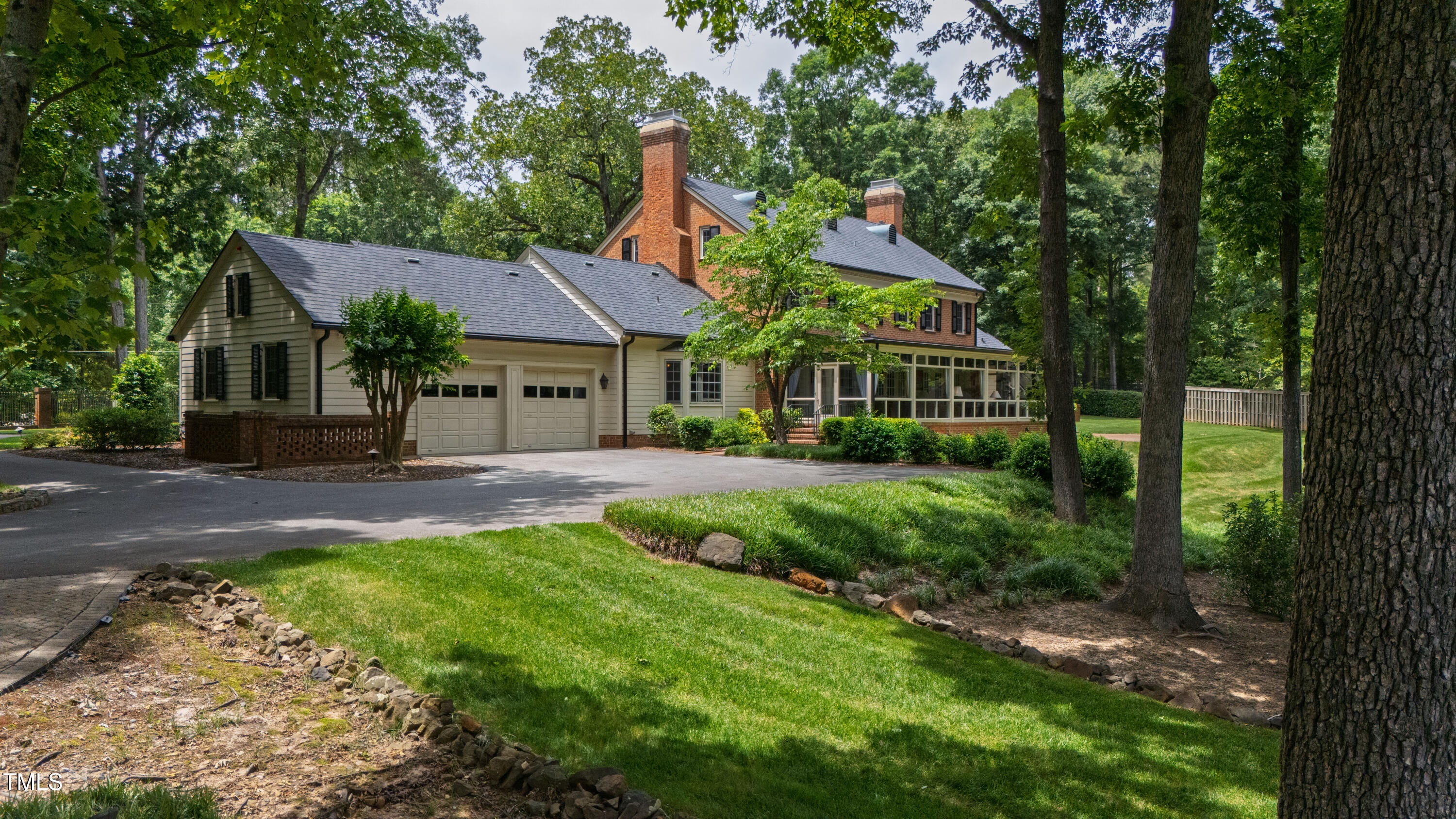 Two-story brick and siding home with multiple chimneys, a glass-enclosed porch, and mature trees.