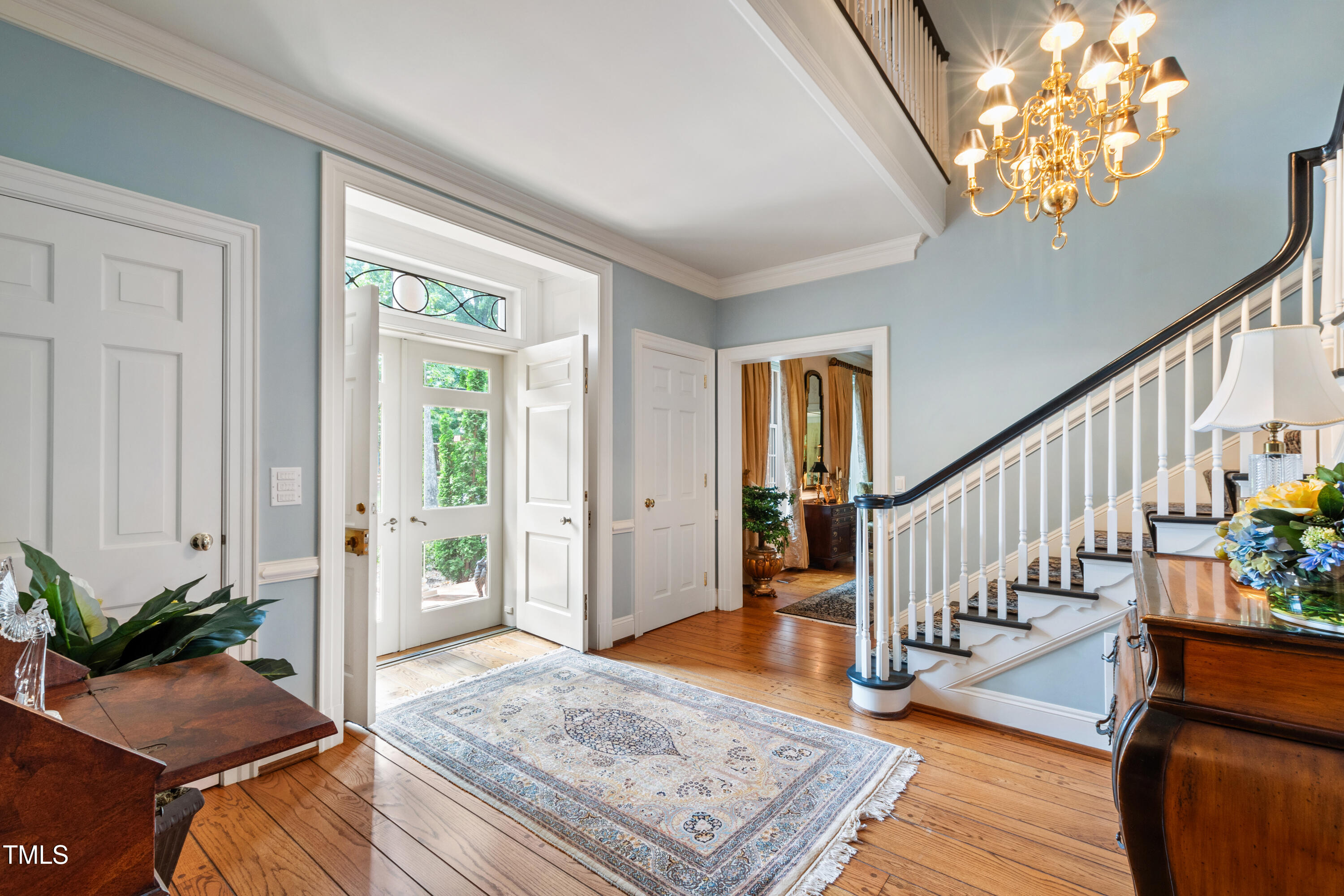 Foyer with a glass-paneled front door, patterned rug, hardwood floors, and a grand staircase.