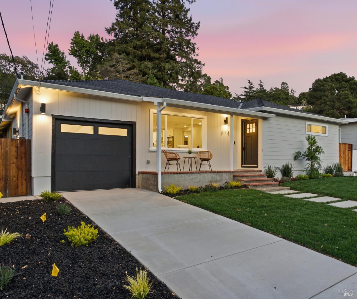 Single-story home with dark garage and warmly lit entry at dusk.