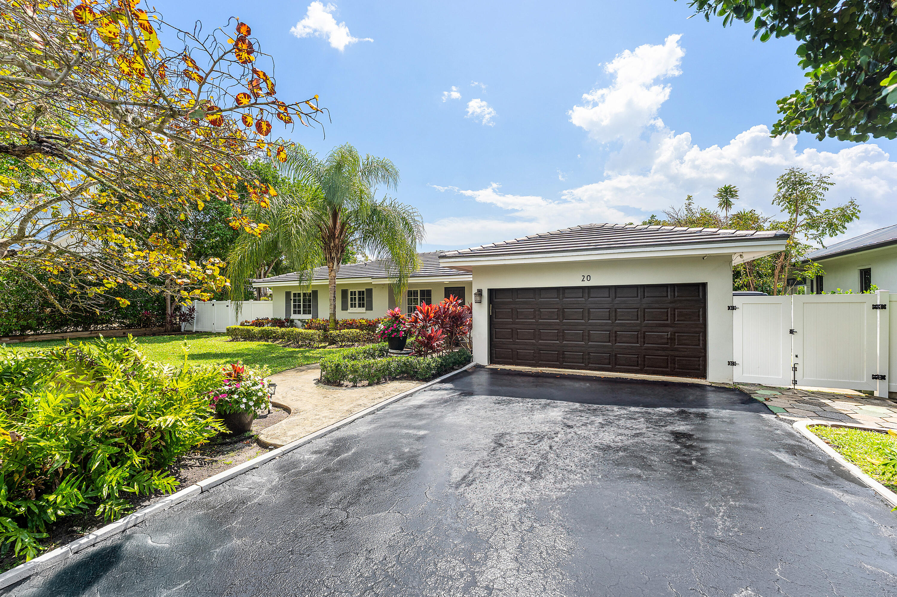 Single-story home with a dark double garage door, wide driveway, and tropical landscaping.