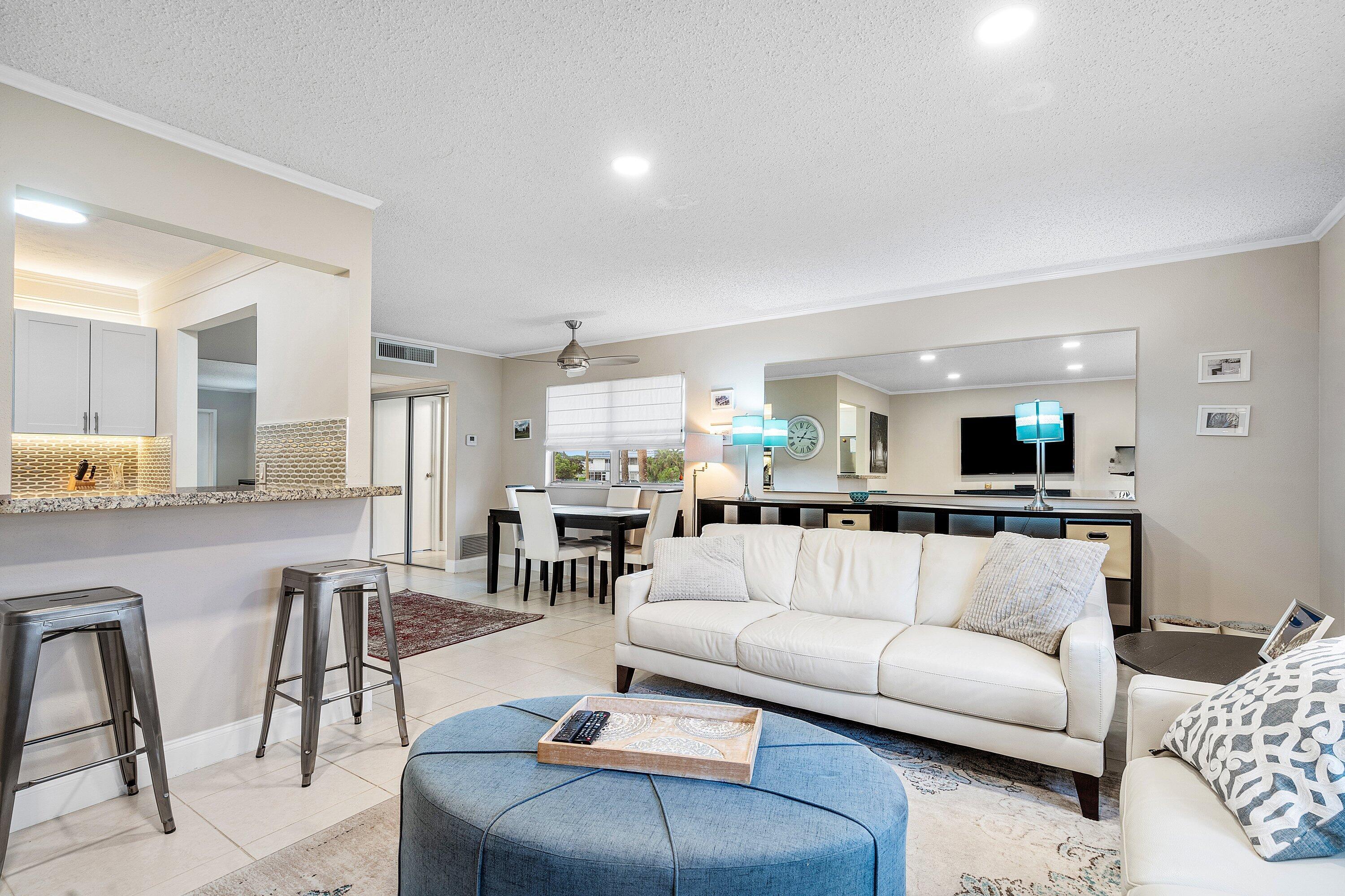 Open-plan living room with a white sofa, blue ottoman, dining table, and breakfast bar.