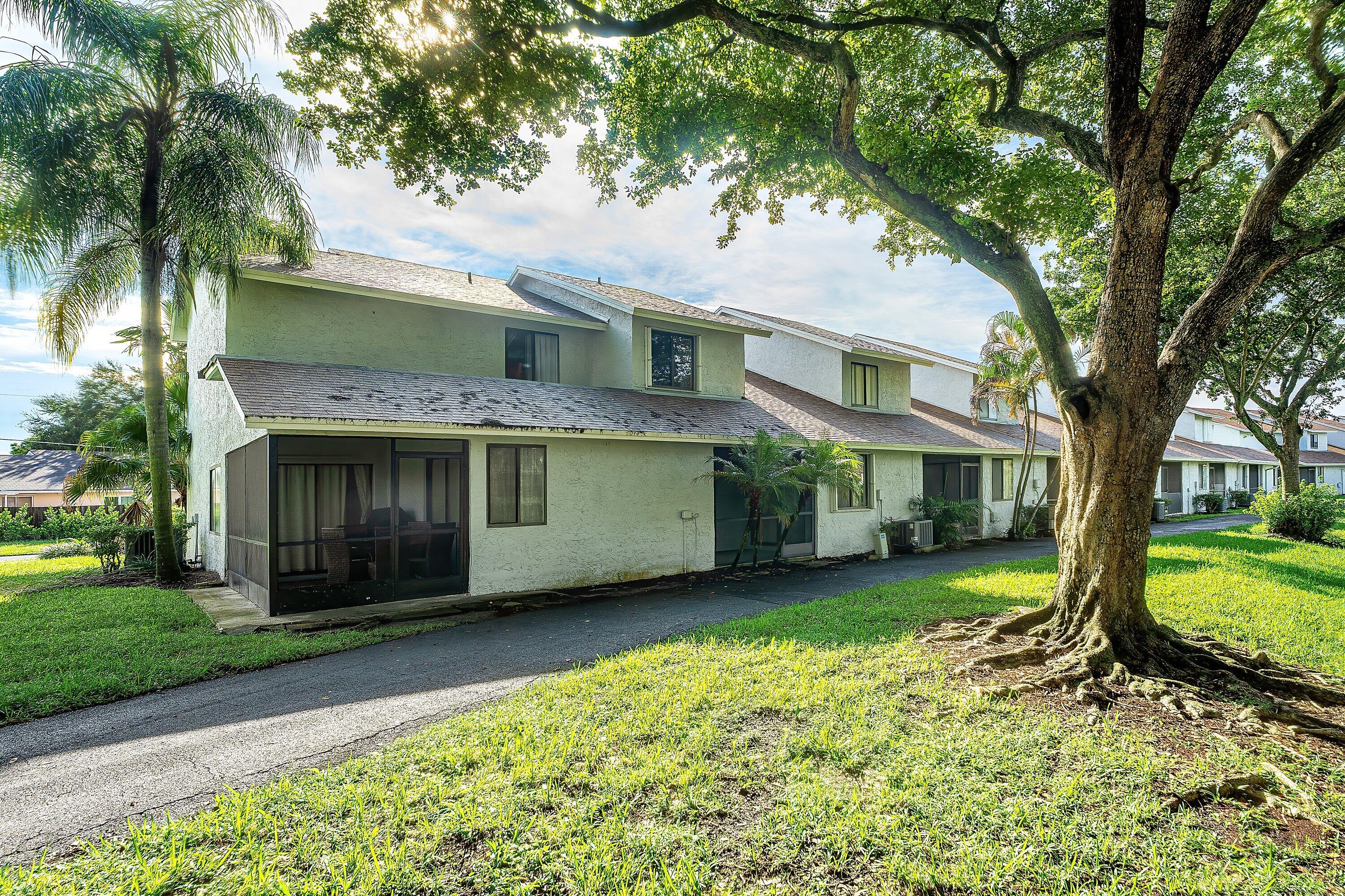 Two-story townhouse with a screened patio beneath large shade trees and palm trees.