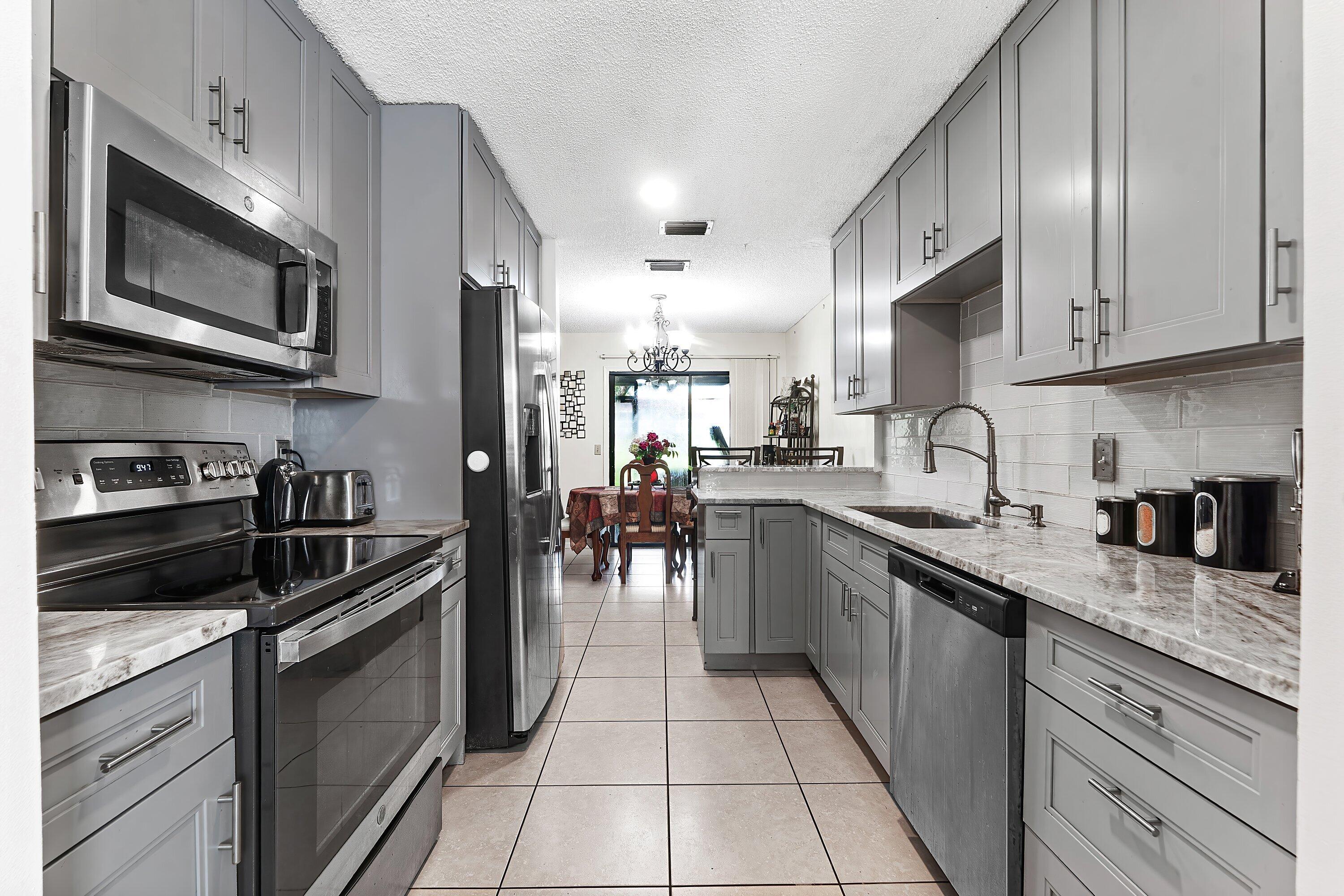Gray galley kitchen with stainless steel appliances, stone counters, and a dining area by the window.