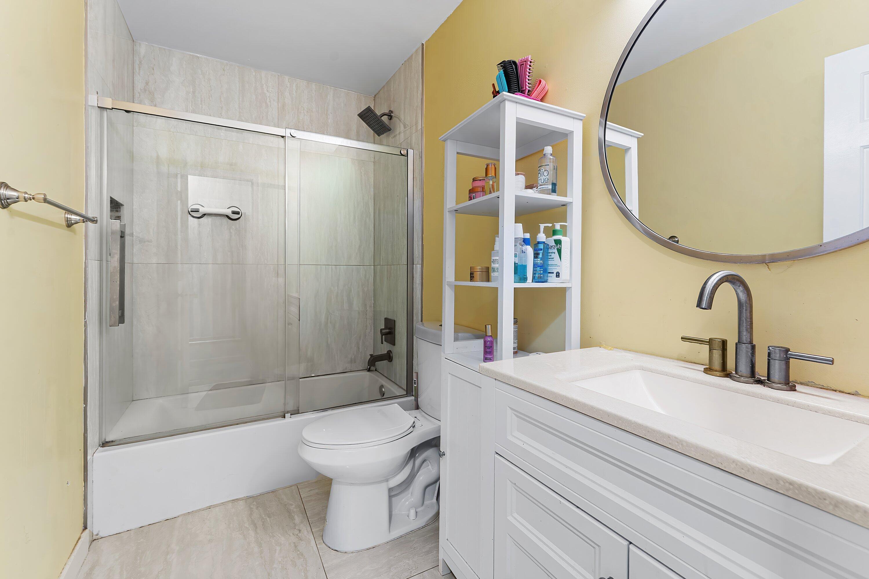 Bathroom with a glass-enclosed tub and shower, white vanity, and large round mirror.