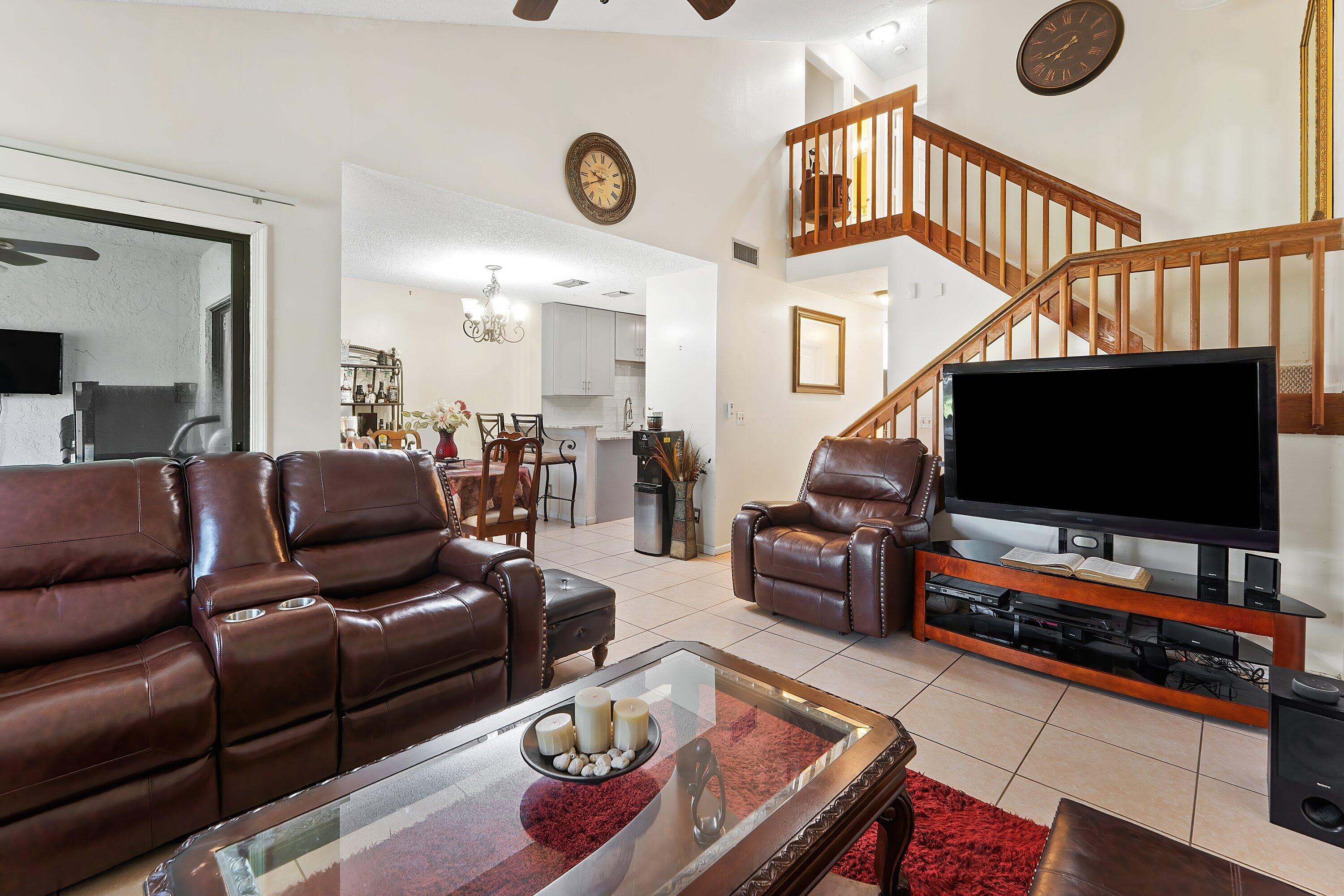 Living room with brown leather seating, a glass coffee table, and a wooden staircase overlooking the open dining area.