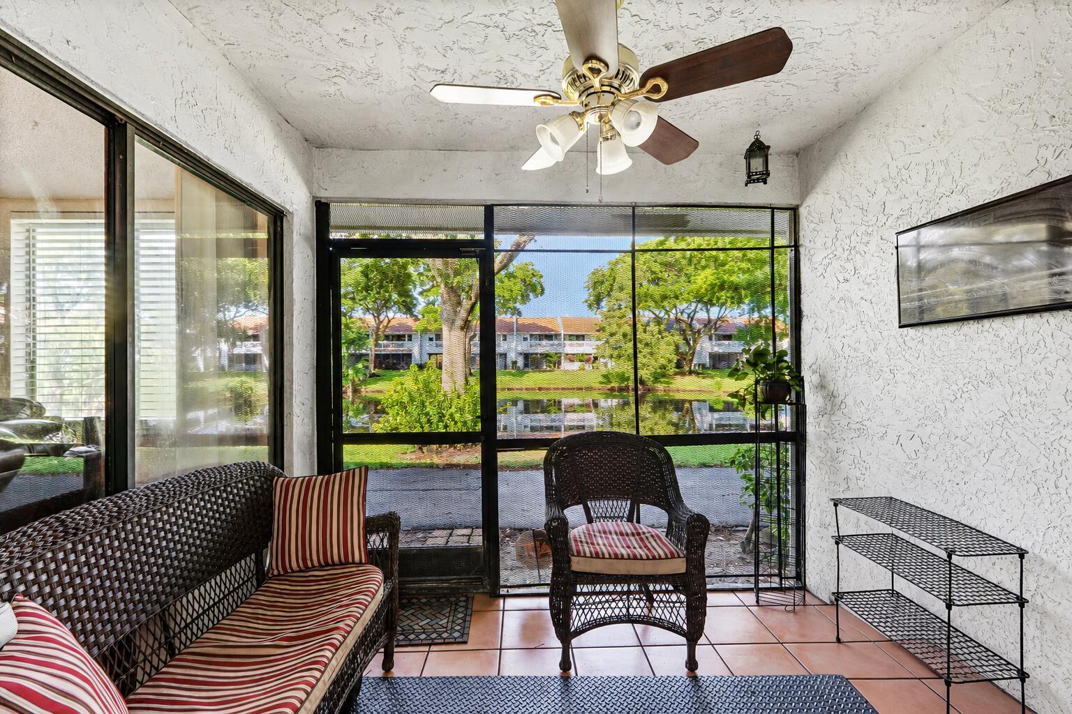 Screened porch with wicker seating and striped cushions overlooking a landscaped pond.
