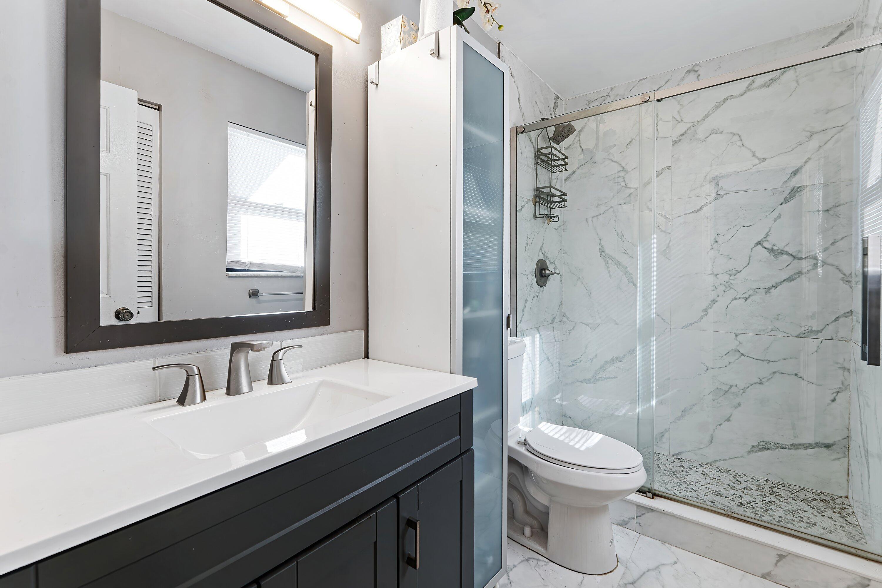 Bathroom with dark vanity and a glass shower lined in marble-look tile.