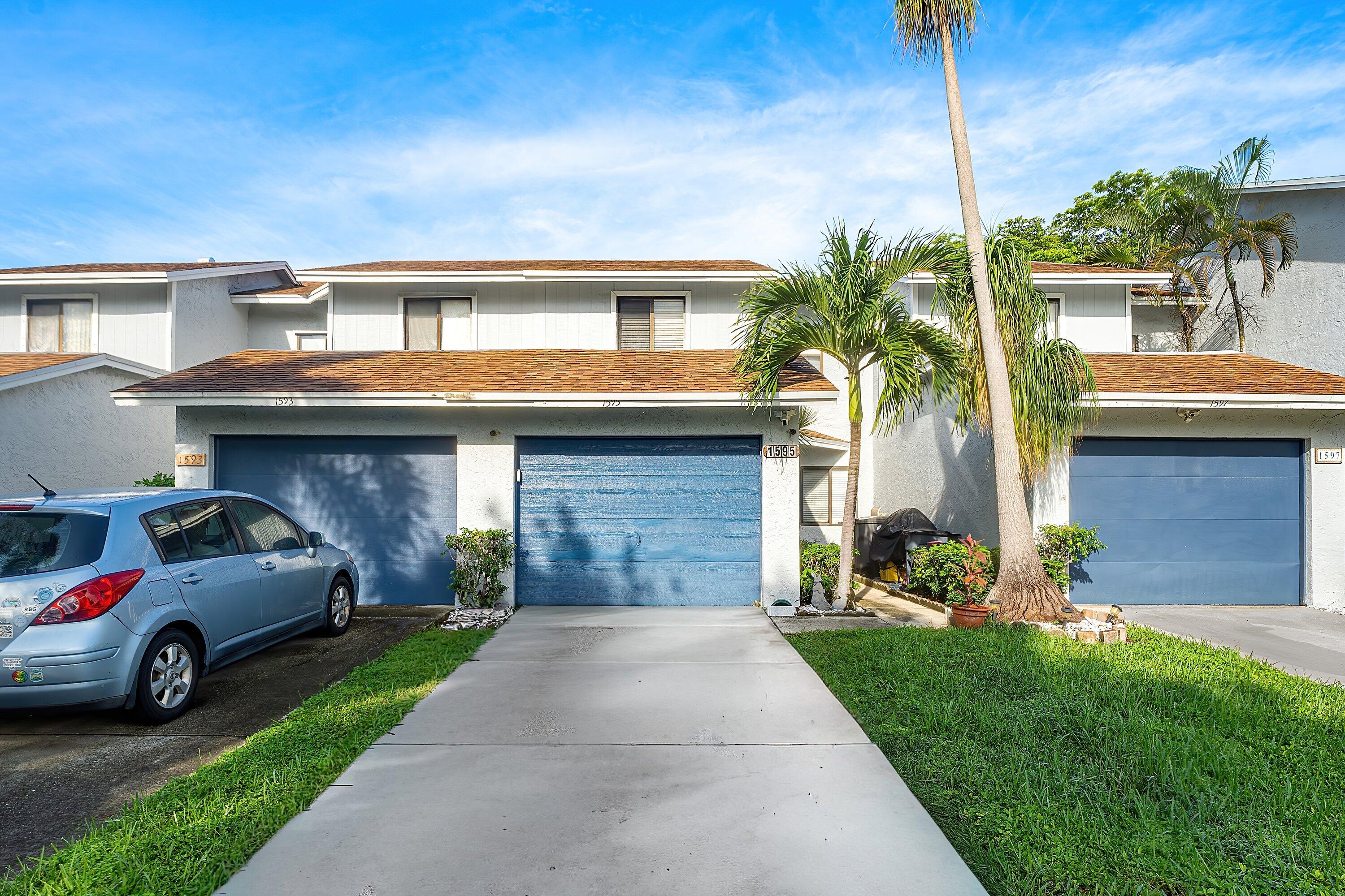 Townhouse exterior with a blue garage door, palm trees, and a concrete driveway.