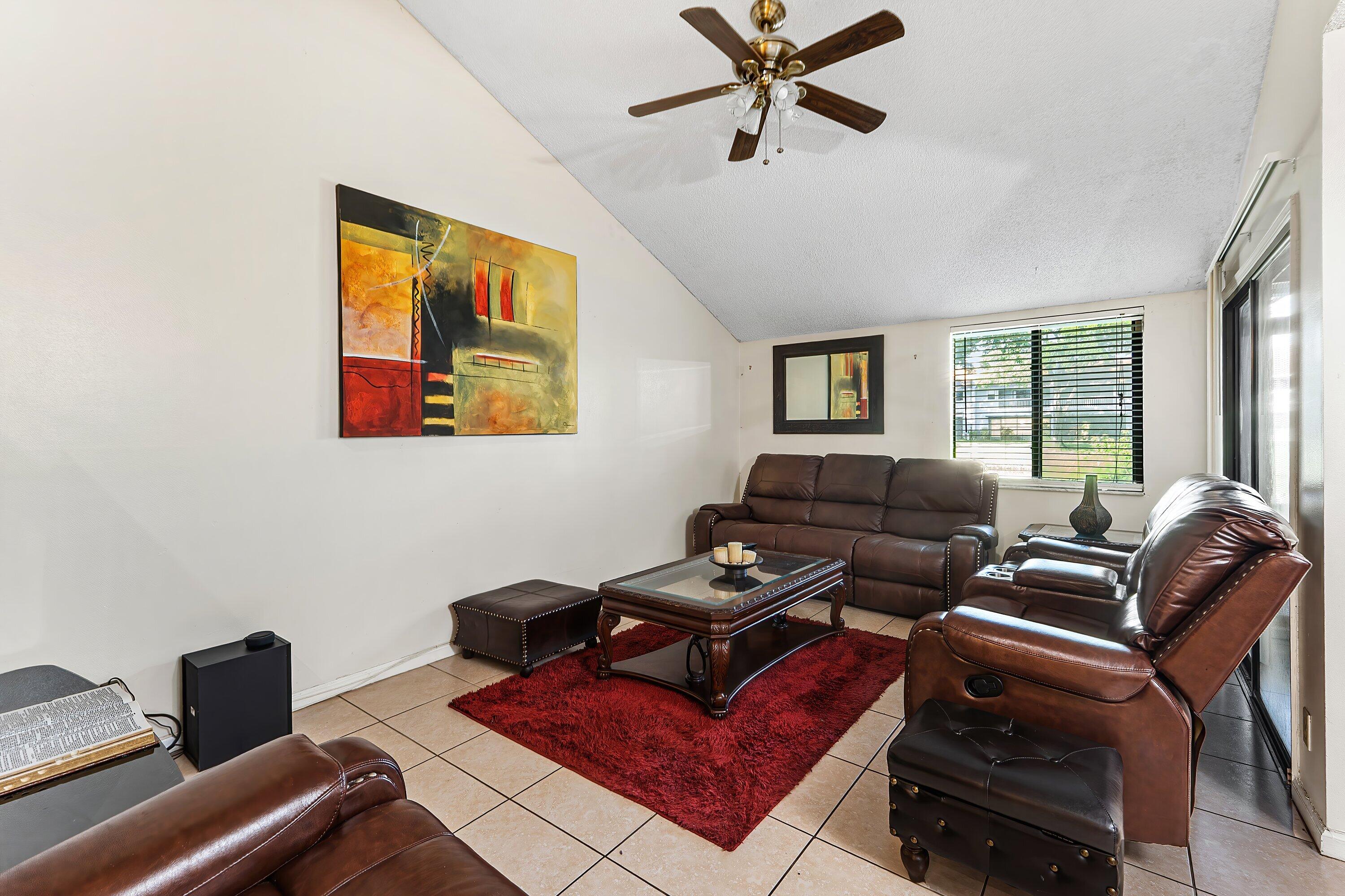 Living room with brown leather seating, a glass-top coffee table, and a deep red rug.