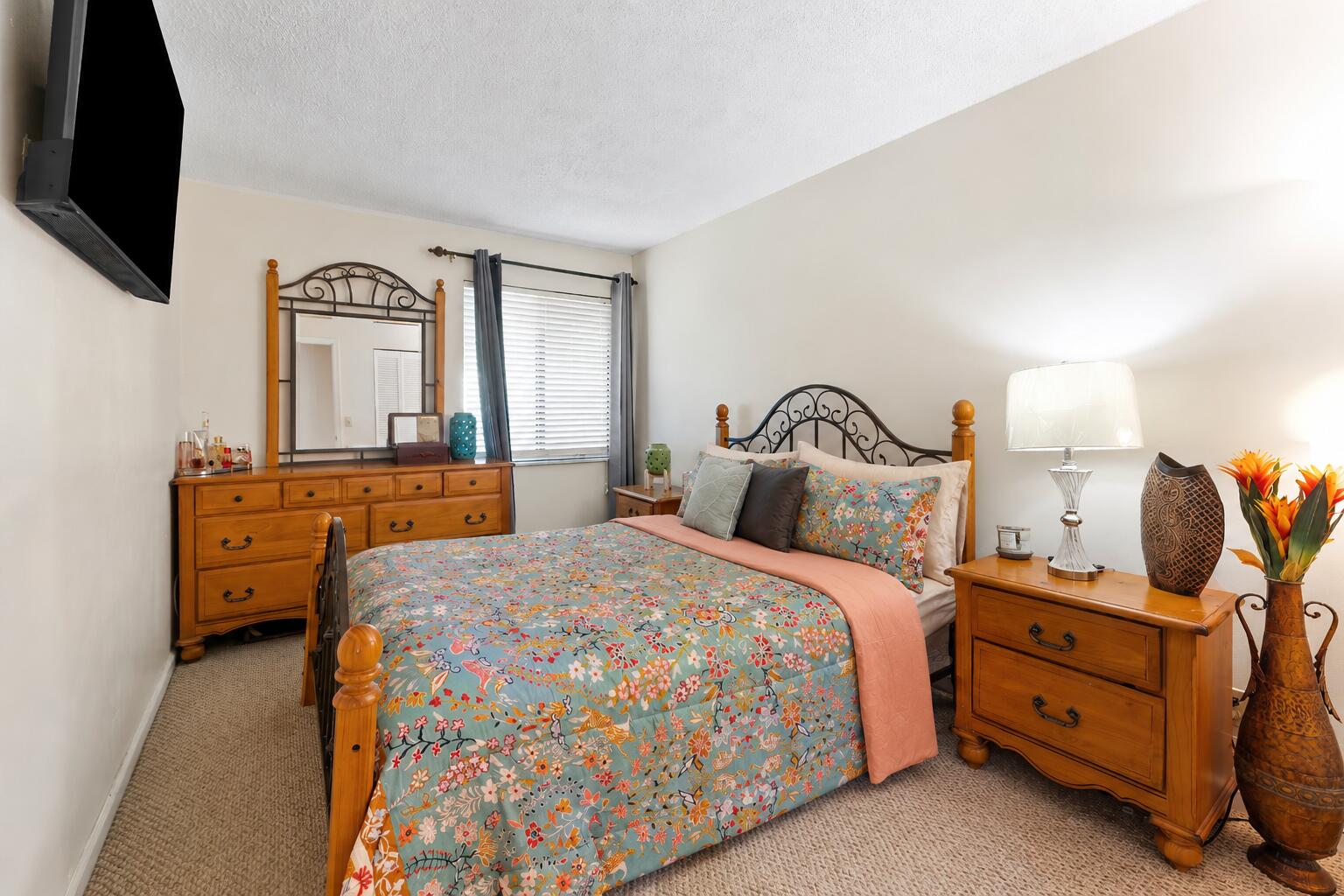 Bedroom with a floral comforter, ornate wooden bed, and matching dressers.