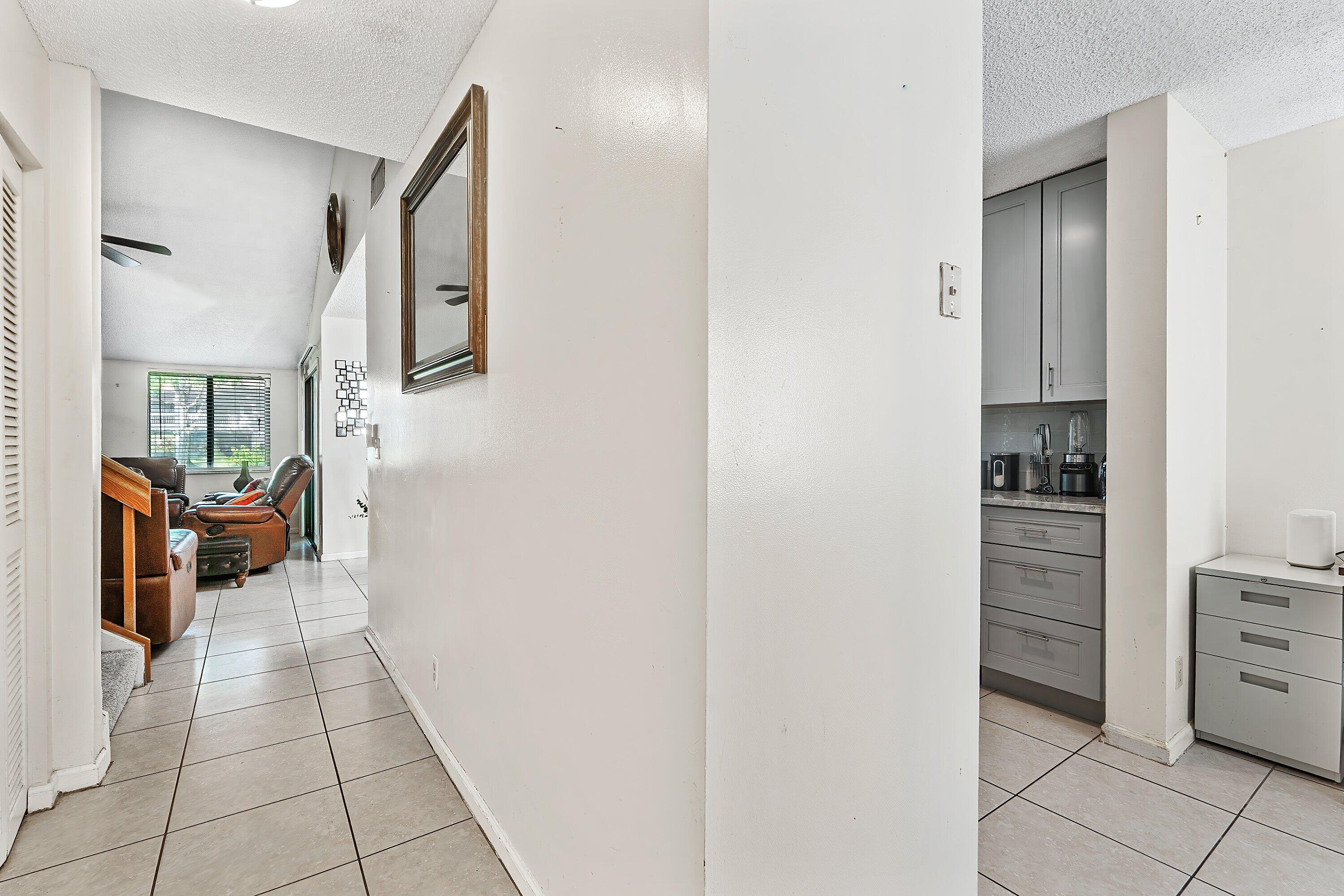 Tiled hallway connecting a furnished living room and a gray-cabinet kitchenette.