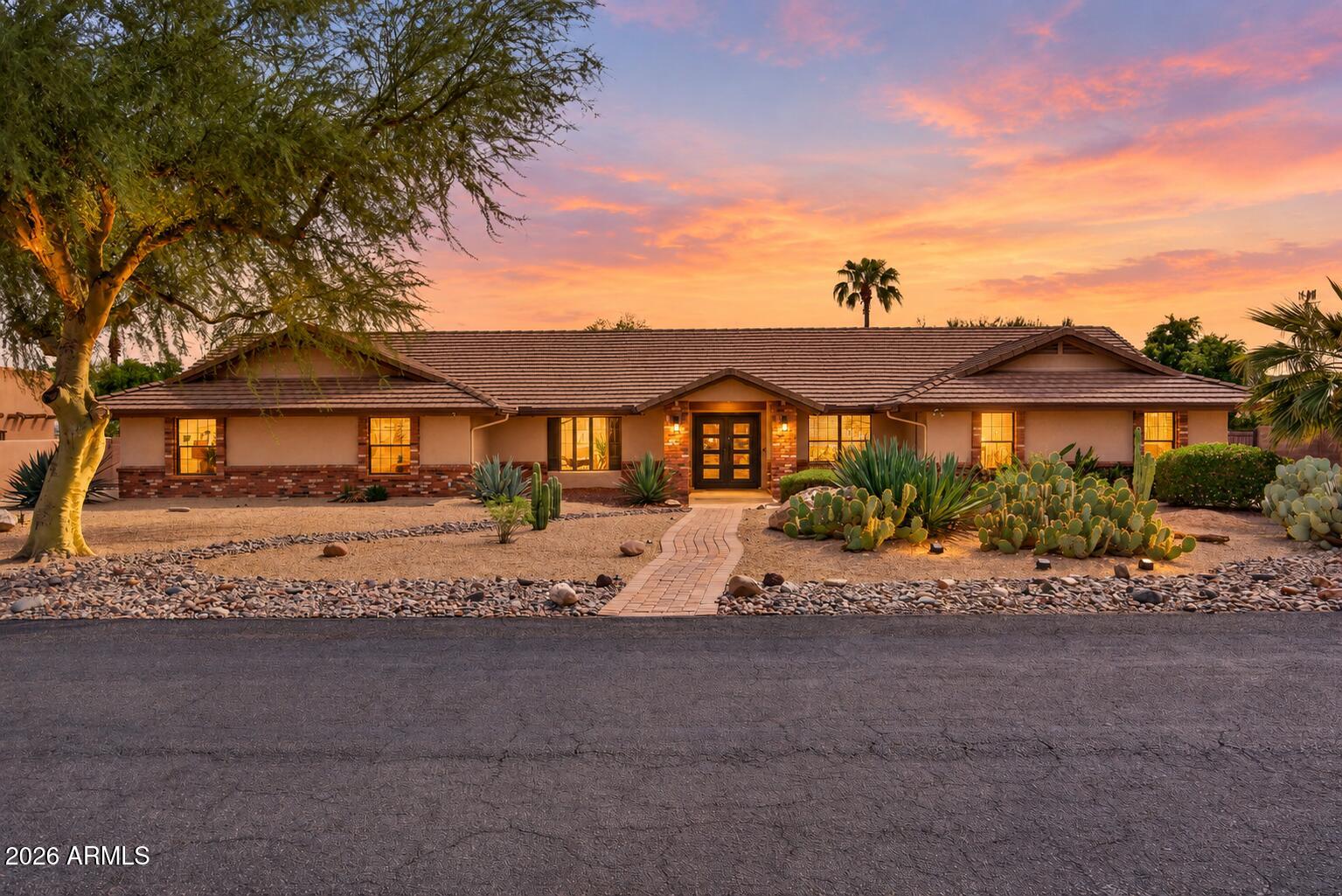 Single-story home with desert landscaping and a curved brick walkway at sunset.