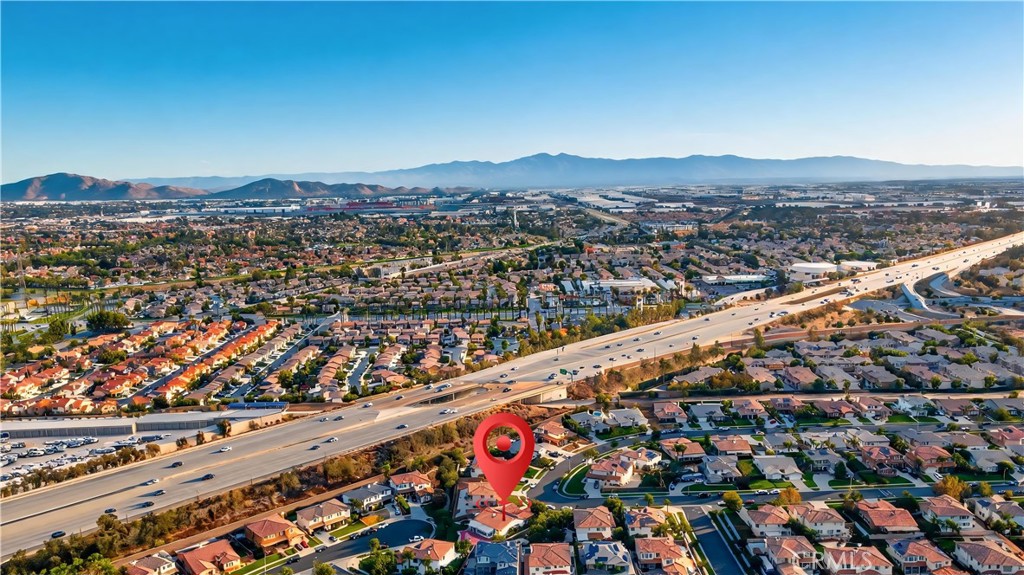 Aerial neighborhood view with a red pin marking a home beside a freeway, with mountains in the distance.