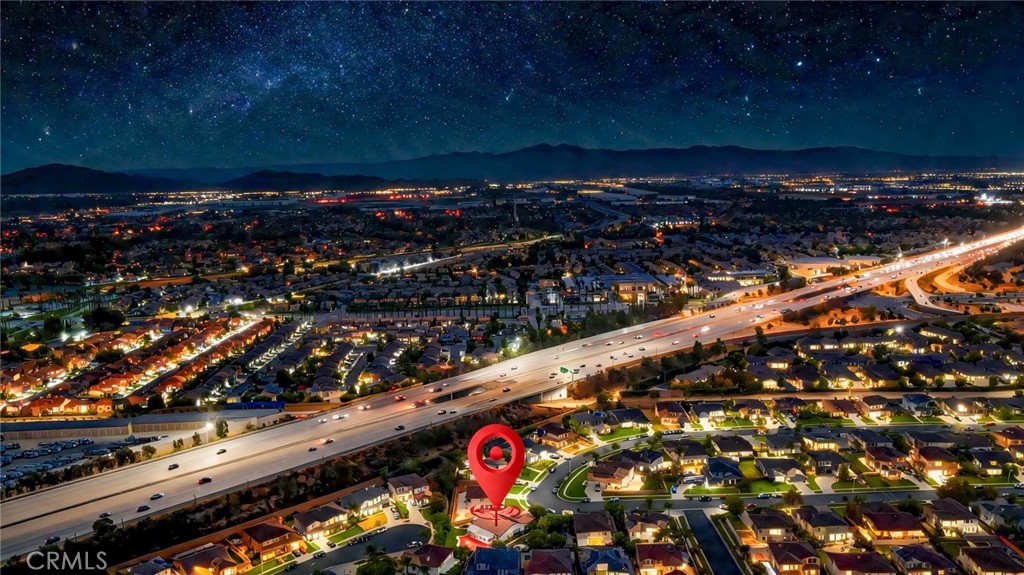 Night aerial of a suburban neighborhood, freeway, distant mountains, and red location marker.