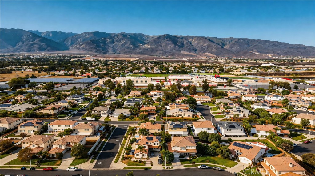 Aerial neighborhood view with detached homes, commercial buildings, and mountains in the distance.