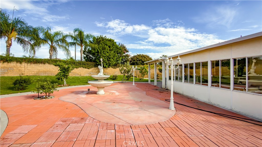 Backyard patio with a tiered fountain, red brick paving, and white lamp posts.