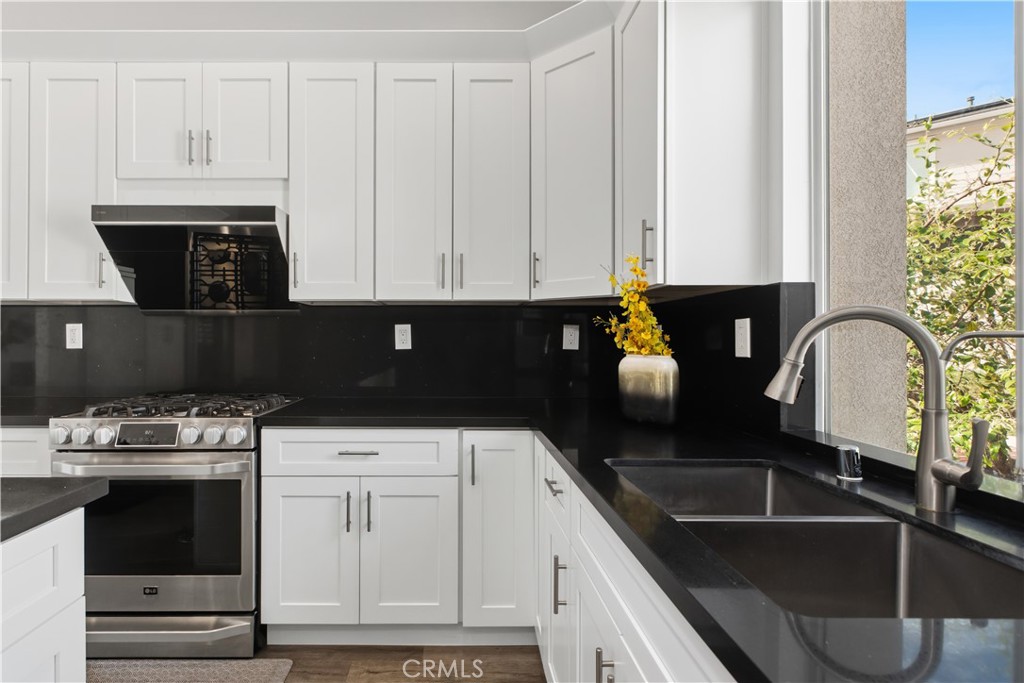 Modern kitchen with white shaker cabinets, black counters, stainless steel range, and double-basin sink by a window.