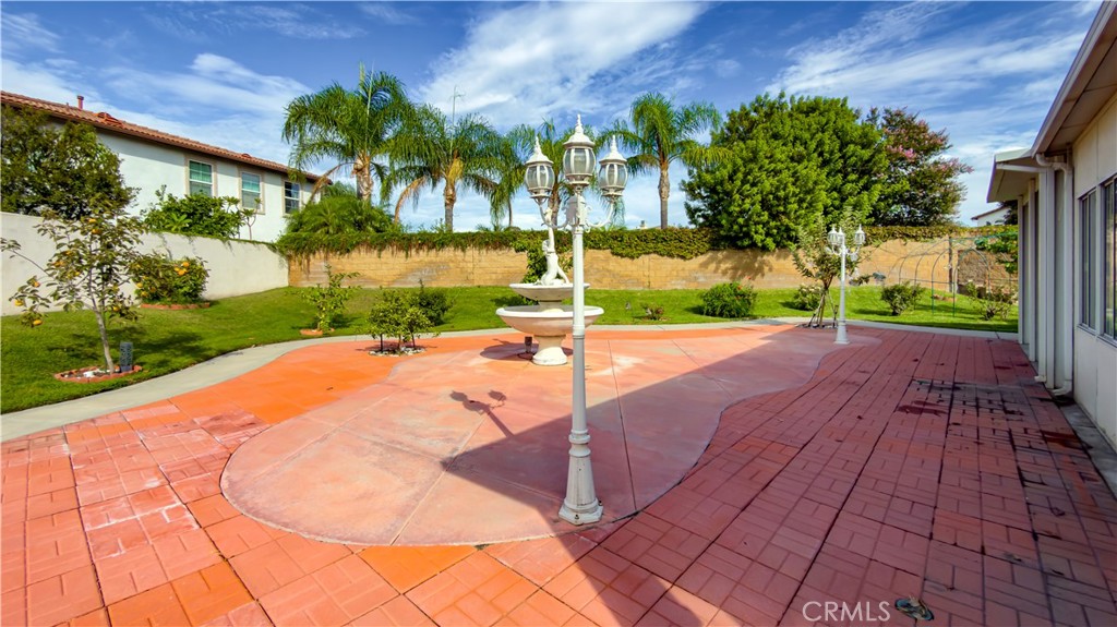 Backyard patio with terracotta paving, a central fountain, decorative lamp posts, and palm trees.