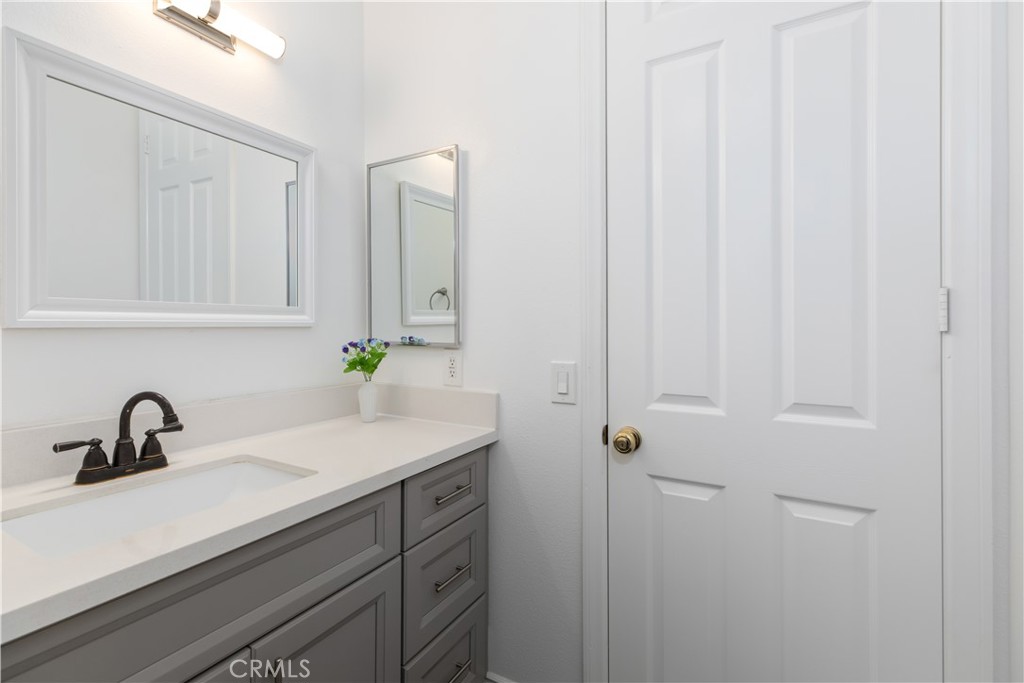 Bathroom vanity with gray cabinets, white countertop, dark faucet, and a small vase of flowers.