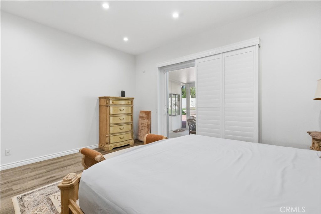 Bedroom with a large bed, wooden dresser, and plantation shutters beside a glass door.