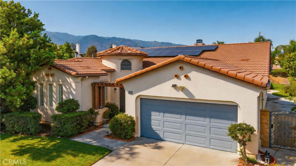 Stucco home with terracotta tile roof, solar panels, and landscaped front yard against a mountain backdrop.