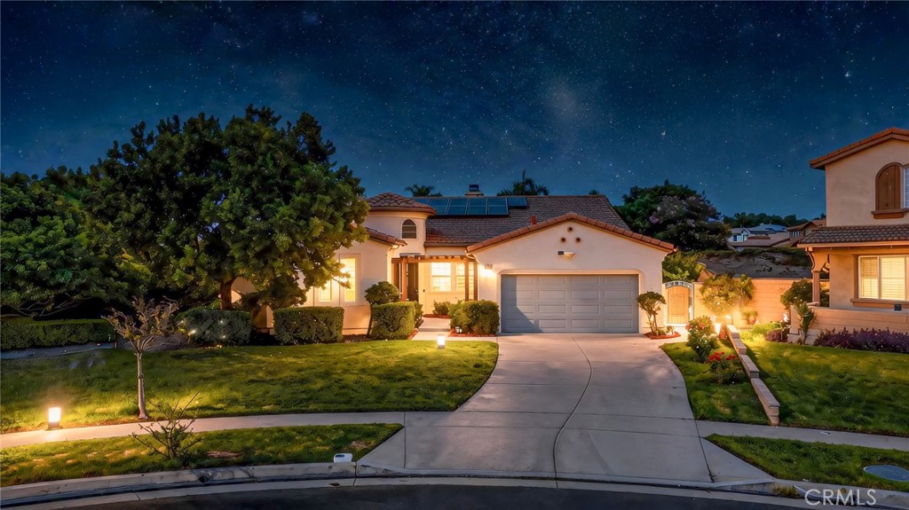 Two-story stucco home with solar panels, landscaped yard, and curved driveway at night.