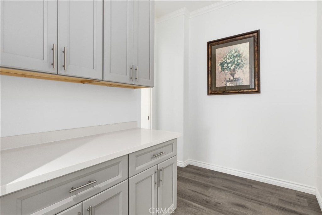 Kitchen with gray shaker cabinets, a long white countertop, and dark wood-look flooring.