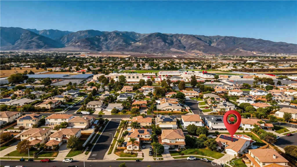 Aerial view of a suburban neighborhood marked by a red pin, with mountains beyond.