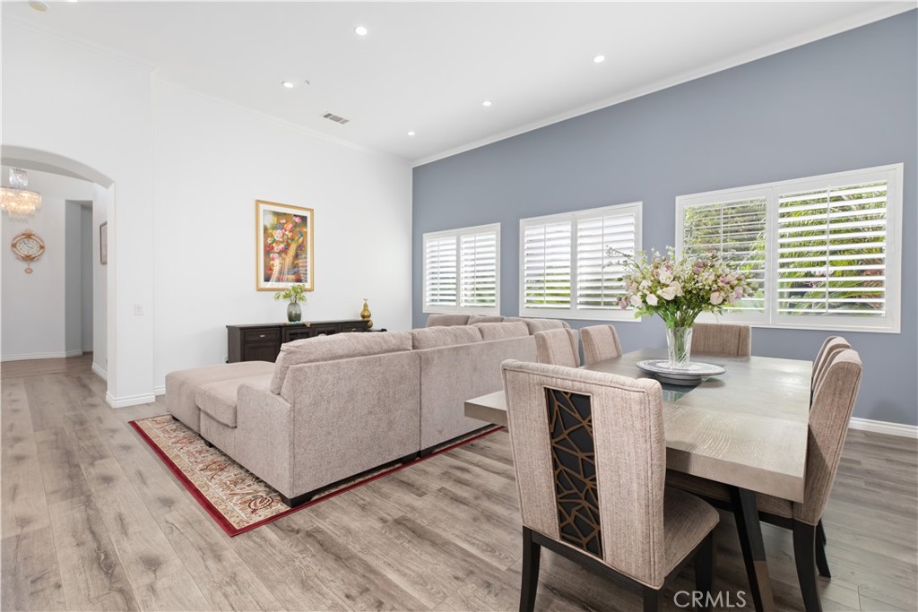 Open-plan living and dining room with a beige sectional, gray accent wall, and plantation shutters.