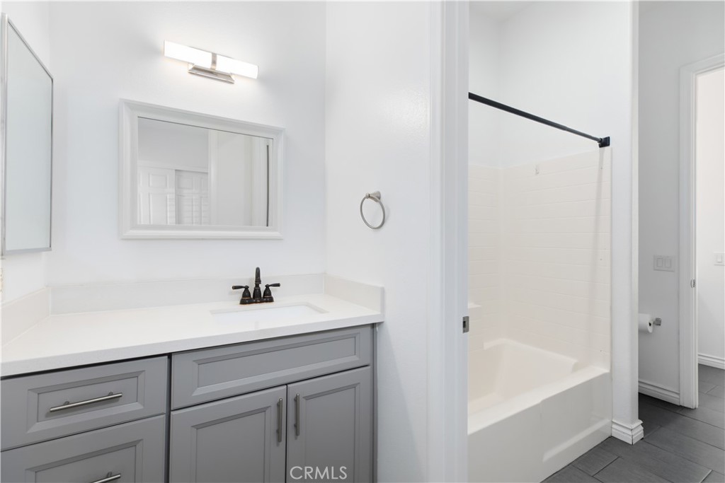 Bathroom with a gray vanity, white countertop, and white tub-shower.