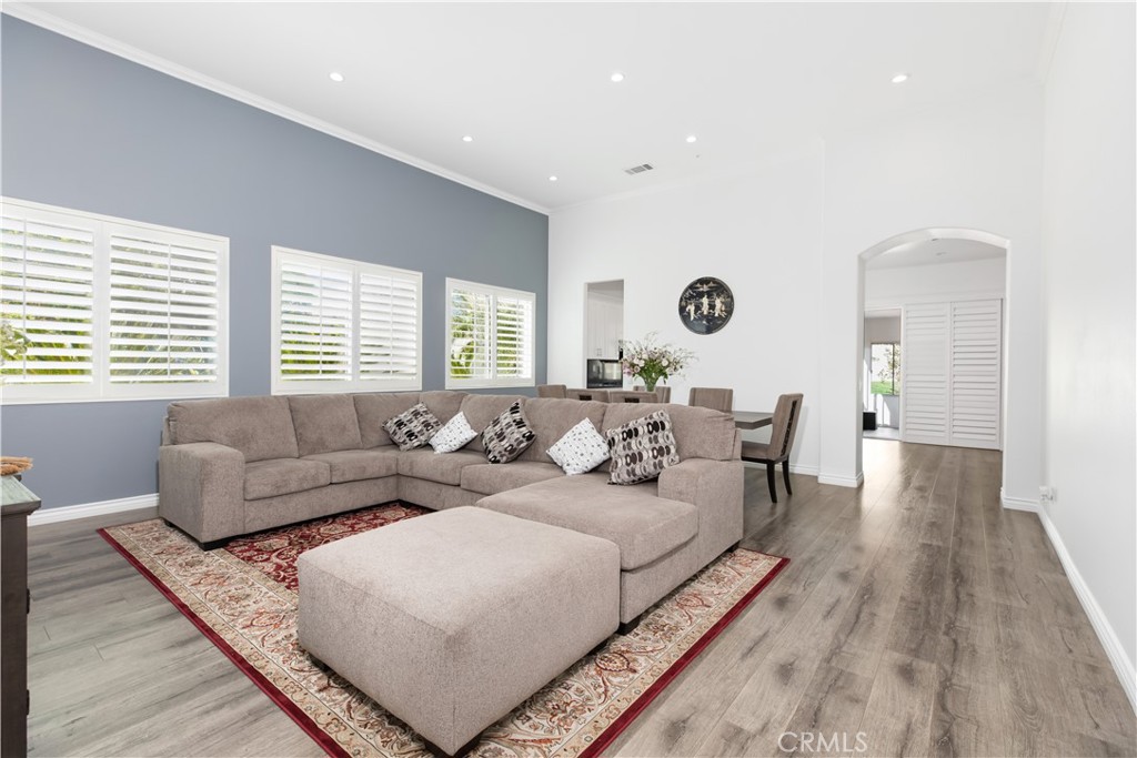 Living room with a sectional sofa and ottoman, patterned rug, shuttered windows, and dining area.