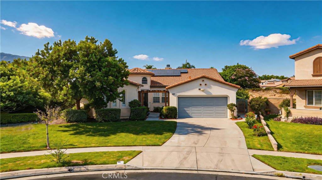 Single-story stucco home with rooftop solar panels, a two-car garage, and landscaped front lawn.