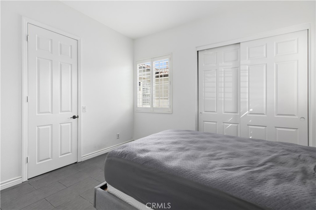 Bedroom with a gray-covered bed, tile flooring, and white sliding closet doors.