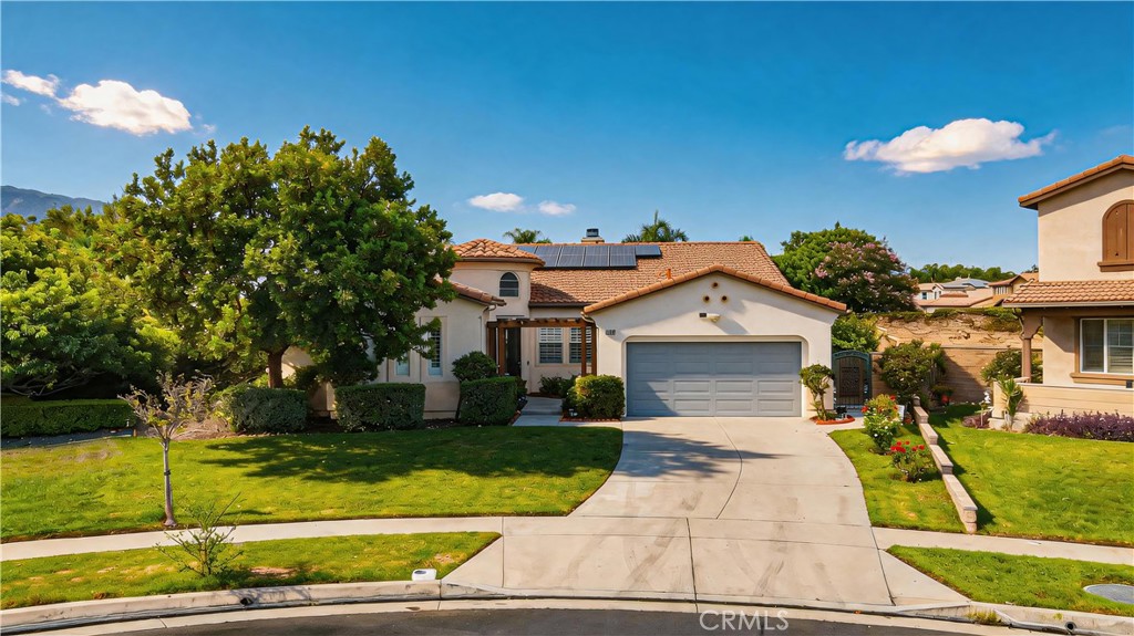 Stucco house with solar panels, a two-car garage, and a curved driveway across a green lawn.