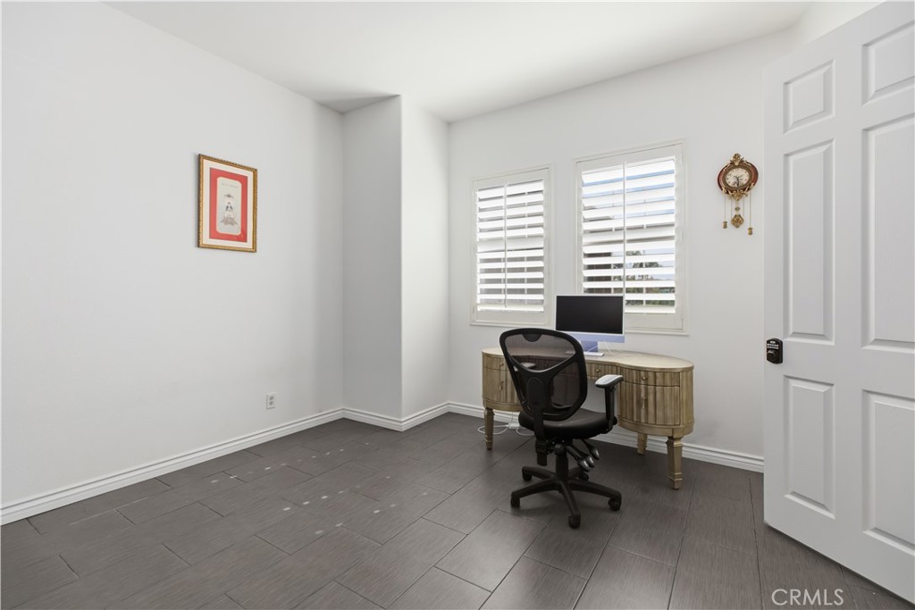 Home office with gray tile flooring, shuttered windows, a curved desk, and a black office chair.