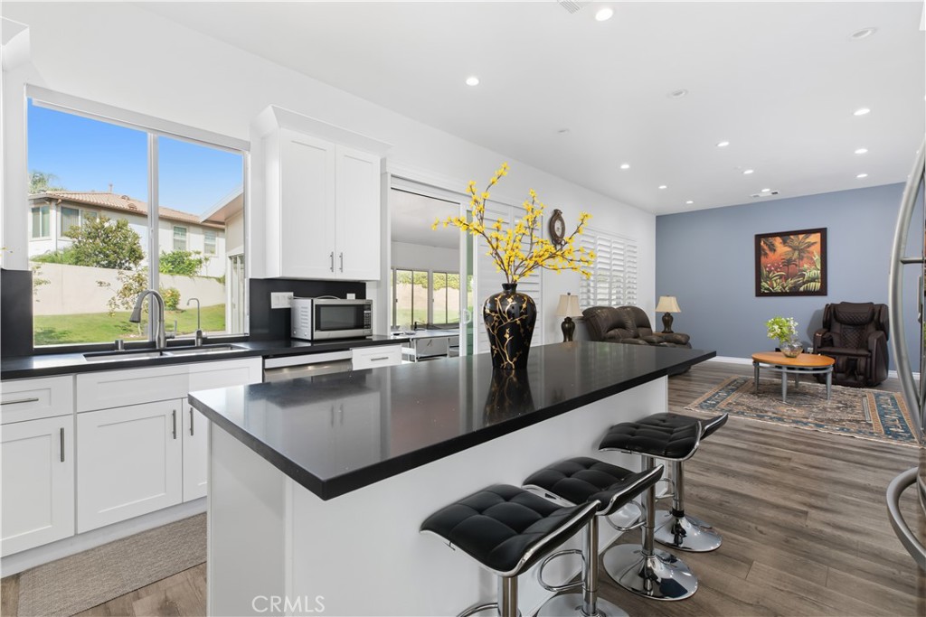 Open kitchen with a long black island and bar stools, adjoining a furnished living area.