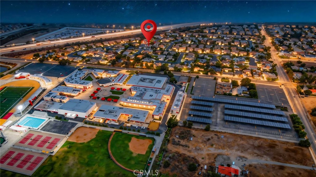 Aerial neighborhood at night, with a red location pin near shopping and sports facilities.