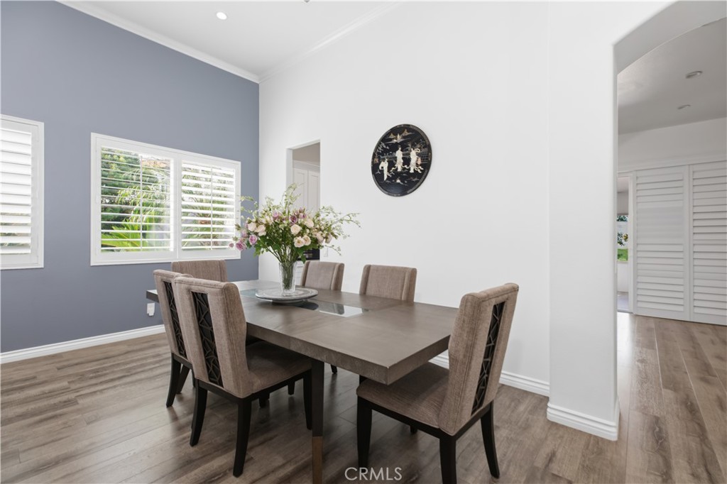 Dining room with a dark wood table, upholstered chairs, and flowers beneath a round wall decoration.