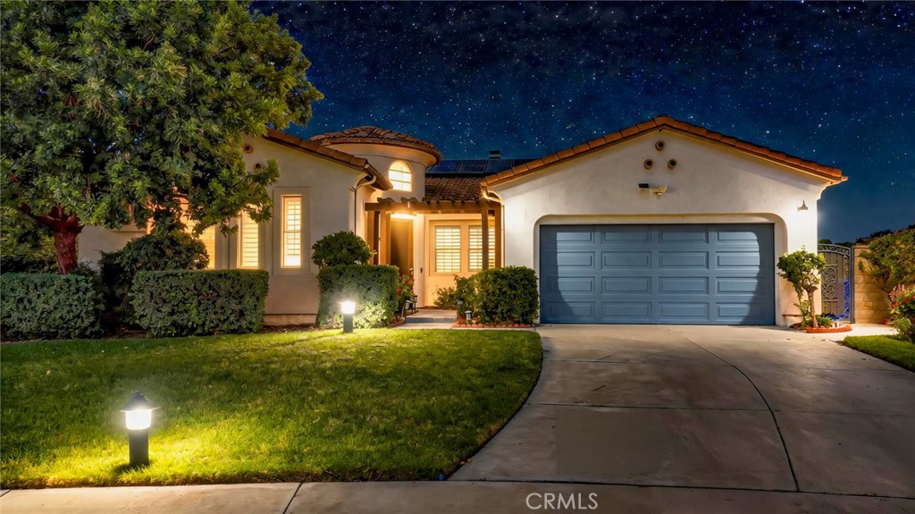 Single-story stucco home with a blue double garage door and illuminated landscaping at night.