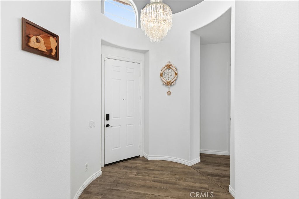 Bright entry foyer with a white front door, curved walls, chandelier, and wood-look flooring.